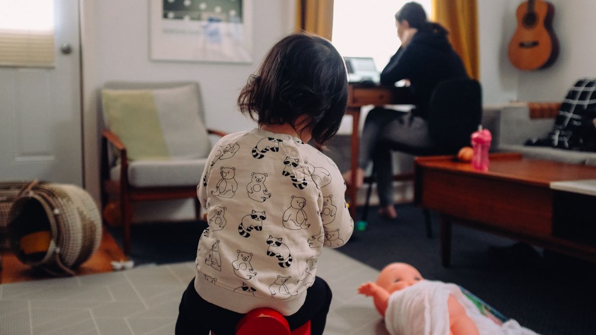 Child playing in the living room while a parent works at a desk in the background